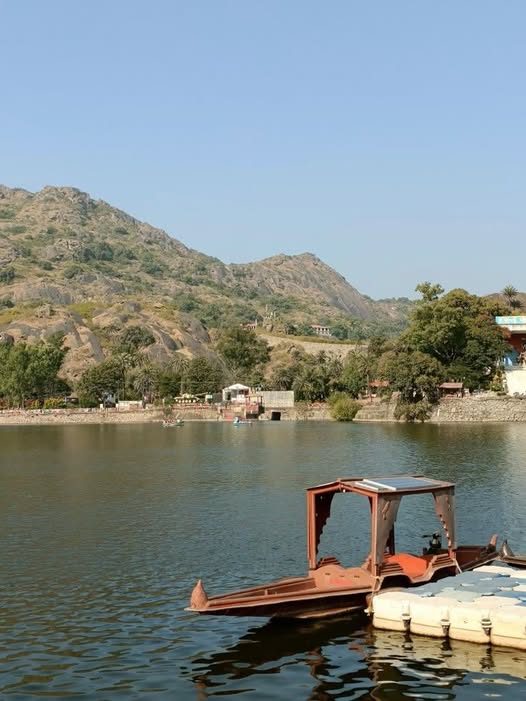 Nakki Lake at sunset in Mount Abu with a small rowboat on calm water and green hills Nakki Lake sunset view during a Mount Abu day trip from Udaipur