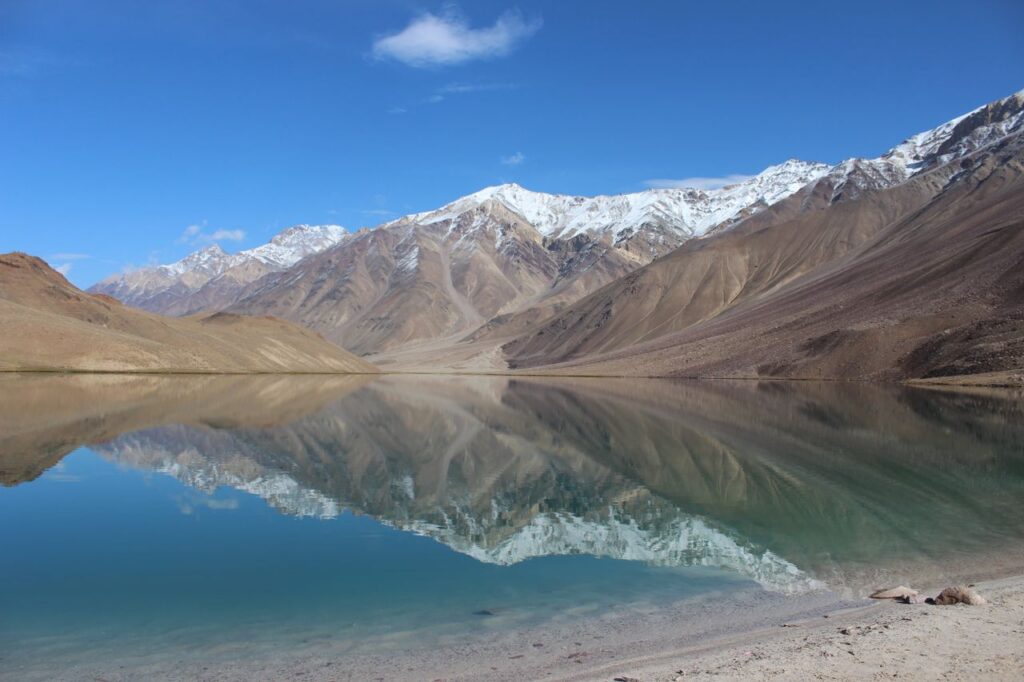 Stunning view of Chandra Taal Lake mirroring the snow-capped Himalayan mountains under a clear blue sky.