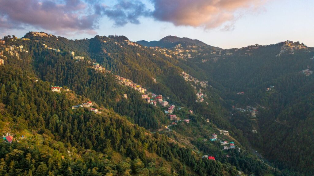 Breathtaking view of Shimla's lush green mountains with scattered houses during sunrise.