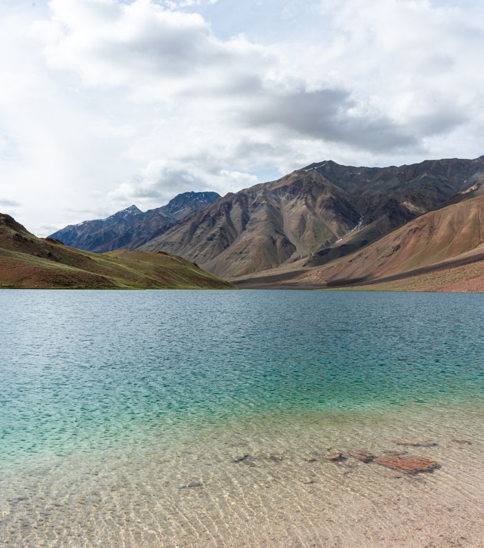 A tranquil view of a pristine lake surrounded by majestic mountains in Himachal Pradesh, India. Chandratal Lake travel guide view of the crescent-shaped moon lake in Spiti