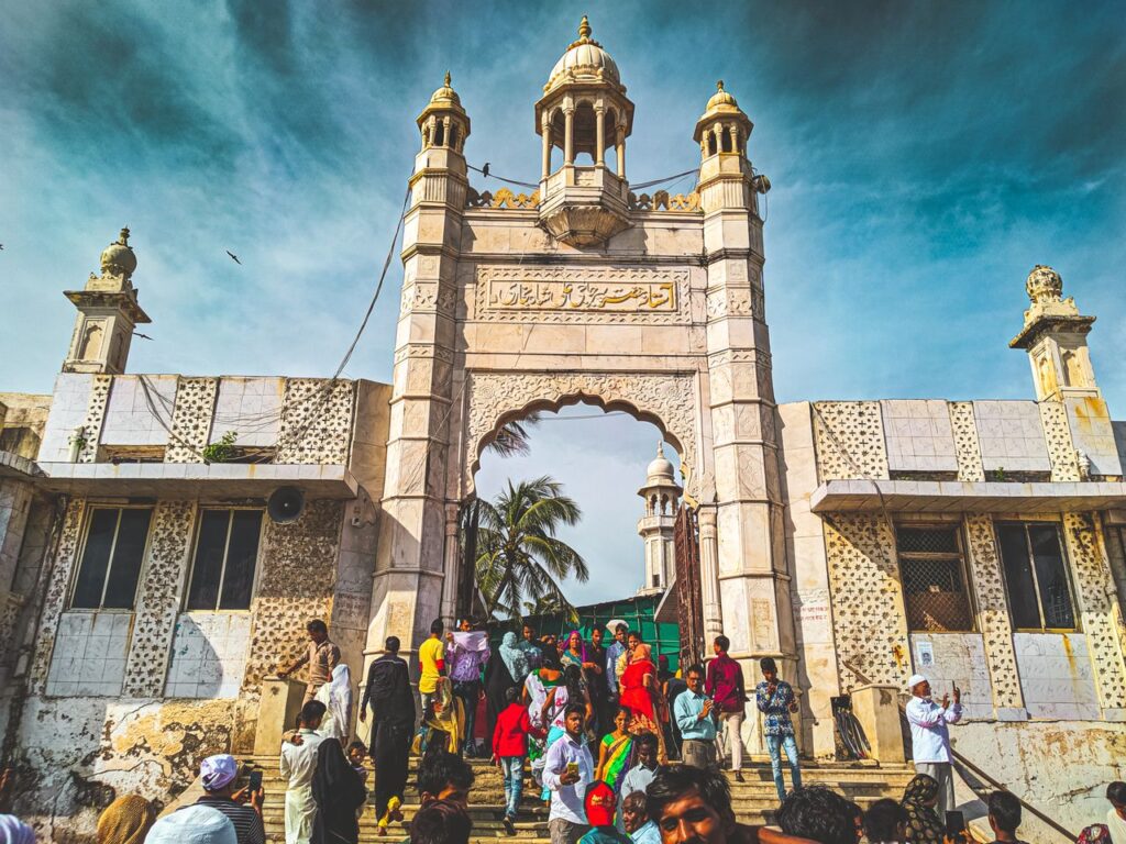 Crowds gather at an ornate historical temple entrance with vibrant cultural architecture.
