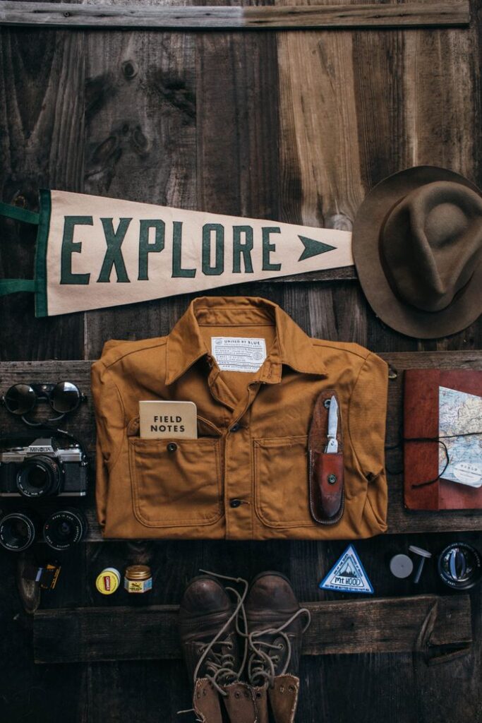 Overhead of vintage photo camera near lenses and sunglasses near shoes and jacket near notebook with map and knife near hat and poster with word explore placed on table Packing list for a Kaza to Hikkim day trip in Spiti Valley