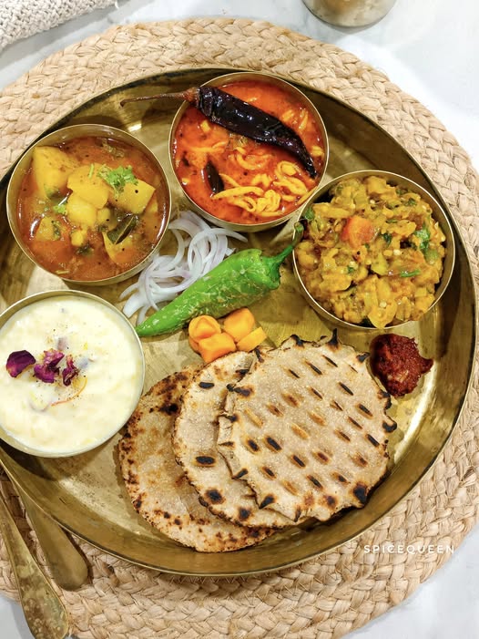 Gujarati-style meal on a table in a casual Goa dhaba. Sev tameta, kadhi, khichdi, rotis and a small salad in steel bowls, warm light, rustic wooden table. Gujarati-style meal at a dhaba, one of the pure veg and Jain restaurants in Goa