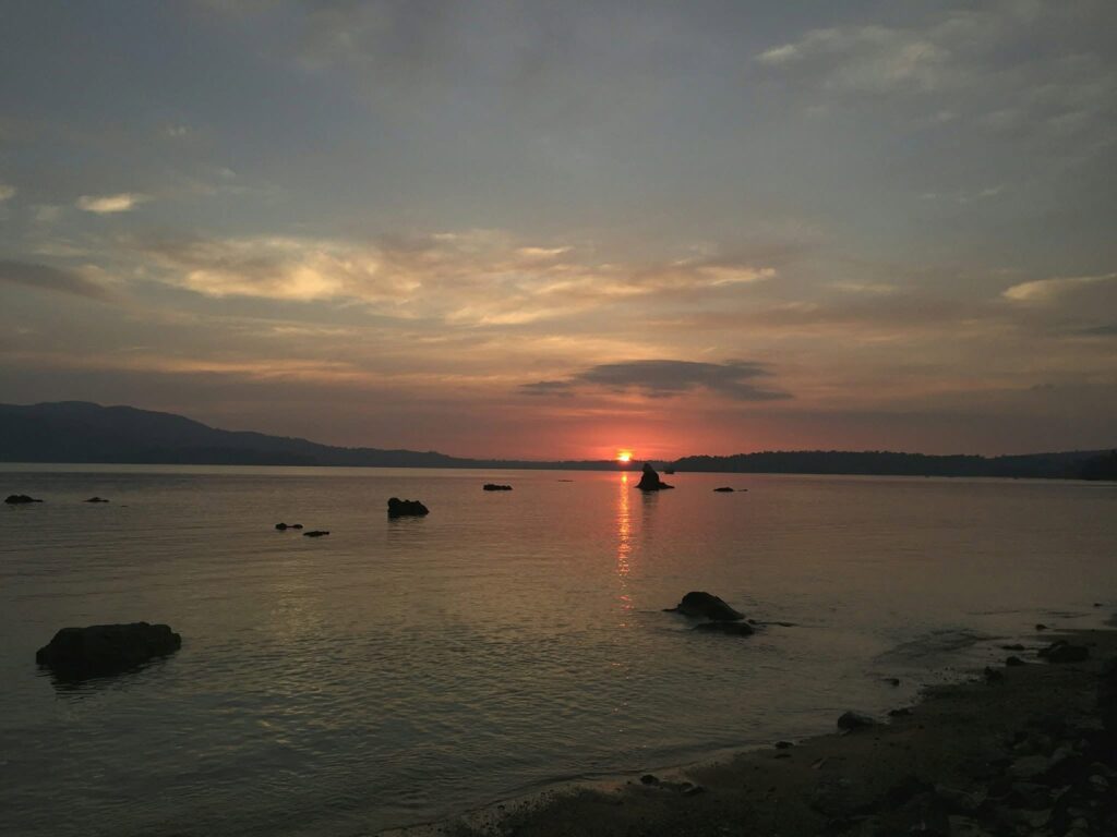 Photorealistic image of a small group of travellers on a rocky Chidiya Tapu shore at sunset, seen from behind as silhouettes, silky waves, orange and purple sky. Travellers watching the Chidiya Tapu sunset near Port Blair